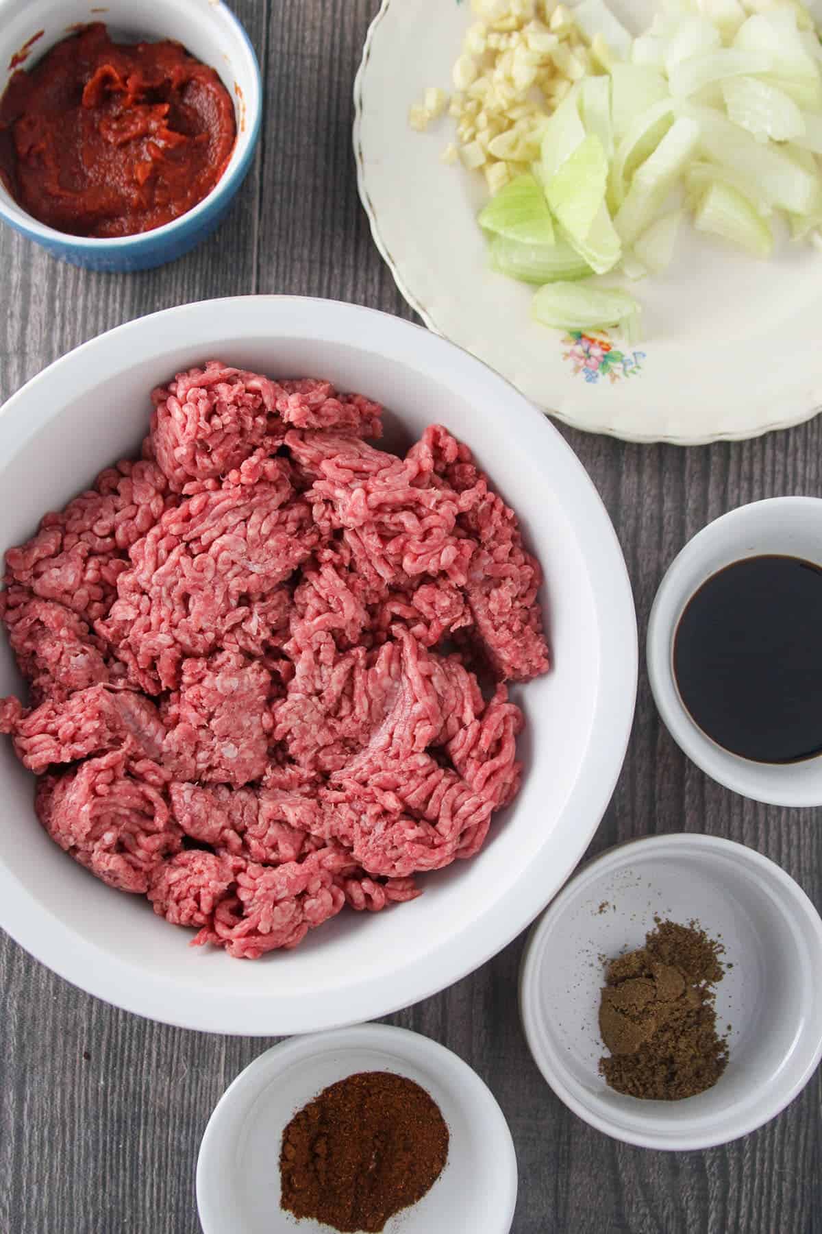 ground beef, soy sauce, chopped onions, tomato sauce, and seasonings in individual bowls