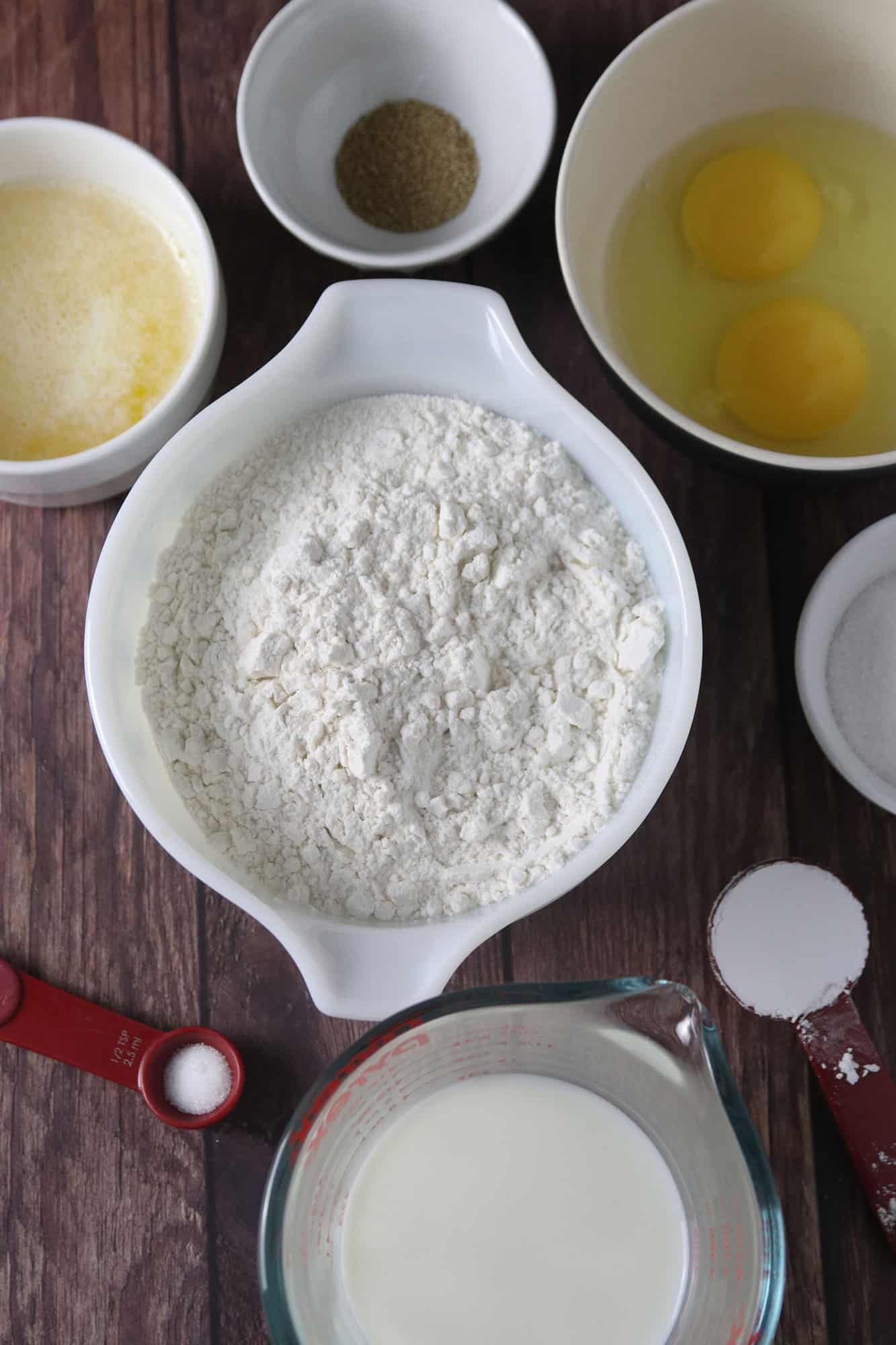 flour, eggs, melted butter, yeast, sugar, milk, salt in bowls