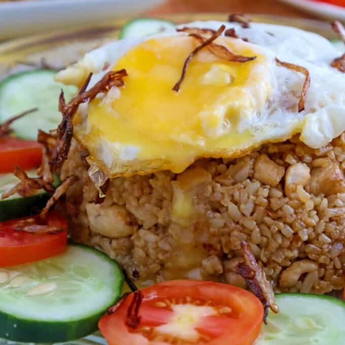 Indonesian fried rice topped with fried egg and garnished with sliced tomatoes and cucumber on a serving plate
