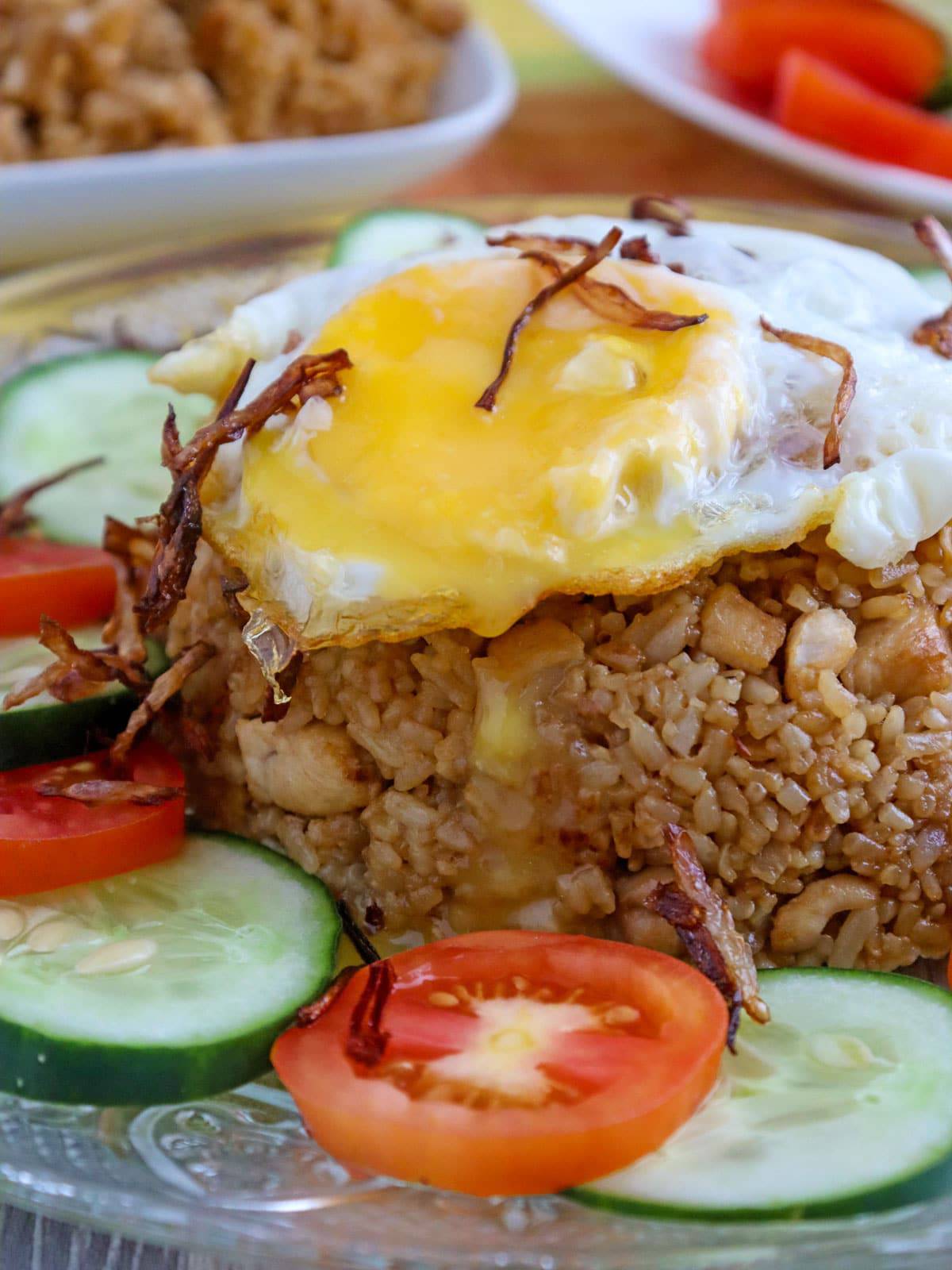 Indonesian fried rice topped with fried egg and garnished with sliced tomatoes and cucumber on a serving plate