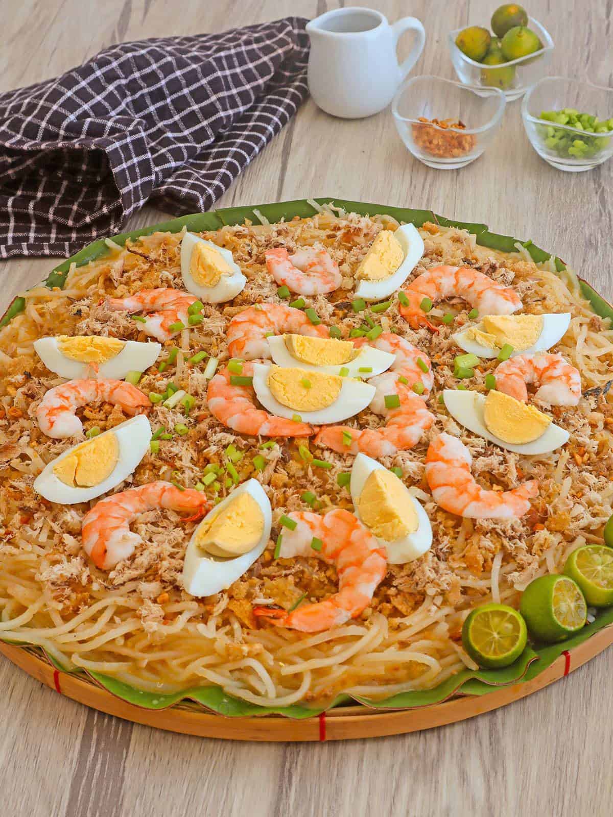 pancit luglug topped with hard boiled slices, shrimp, and chicharon on a wood basket