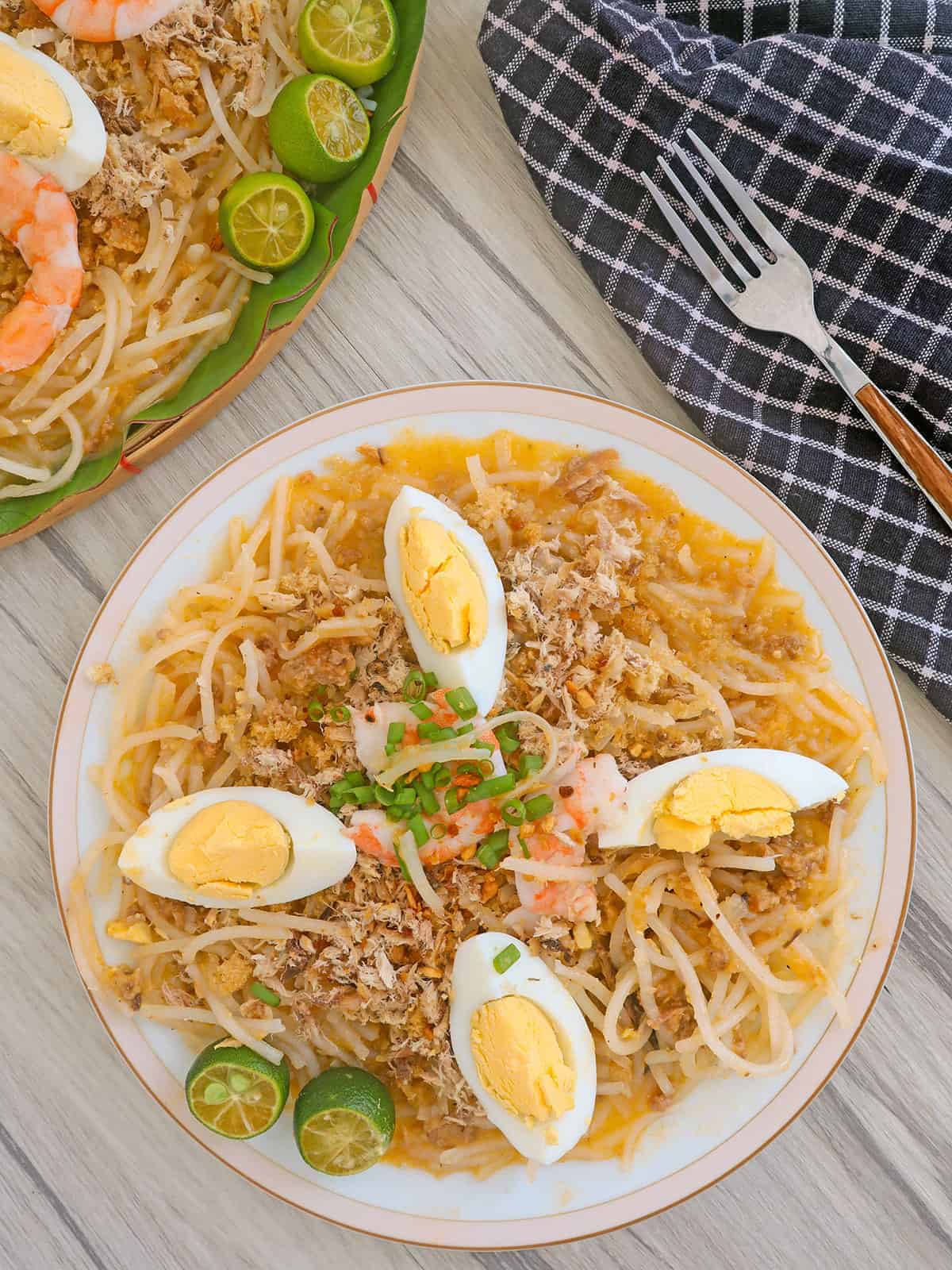 pancit luglug with hardboiled eggs and shrimp on a white plate