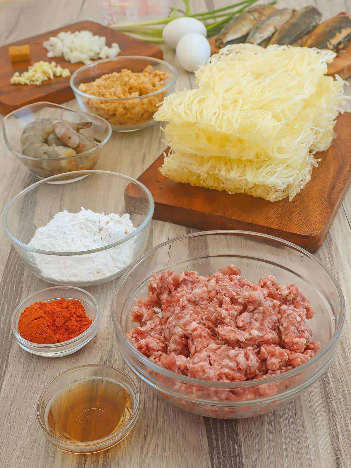 ground pork, cornstarch, cornstarch noodles, crushed chicharon, peeled uncooked shrimp in individual glass bowls and tinapa fish on wood board