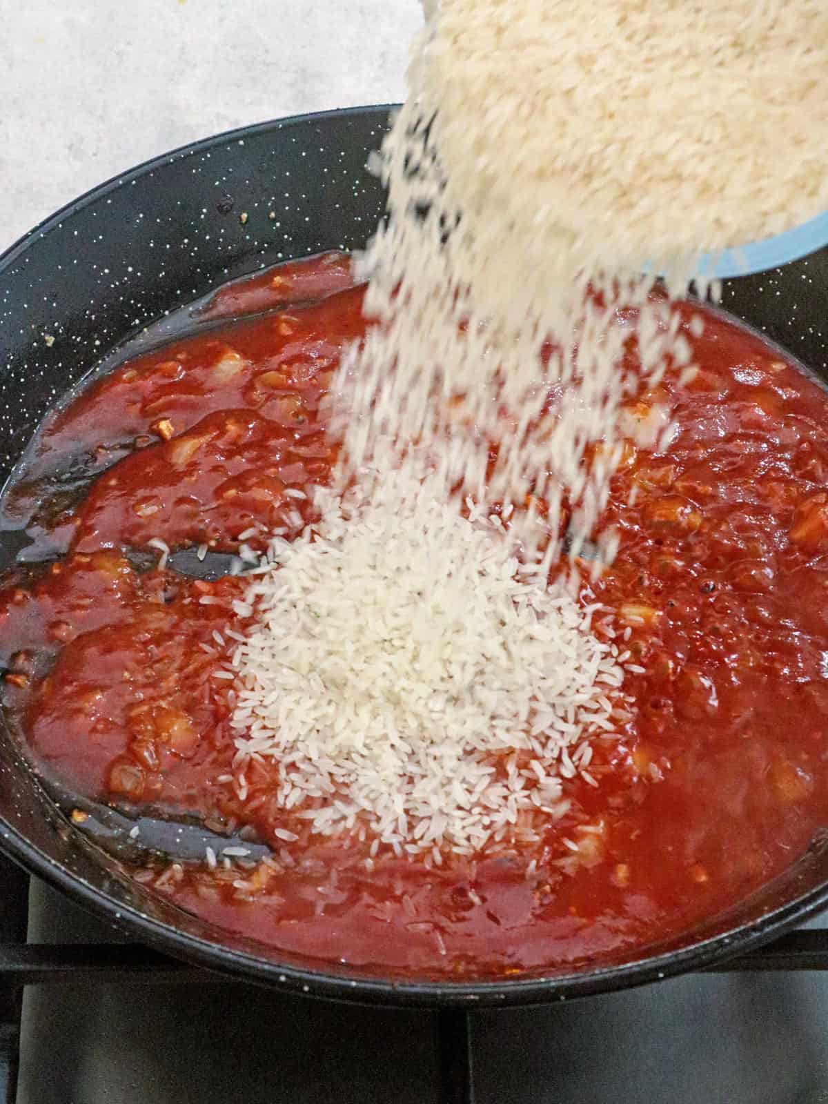 pouring rice to tomato sauce in a pan