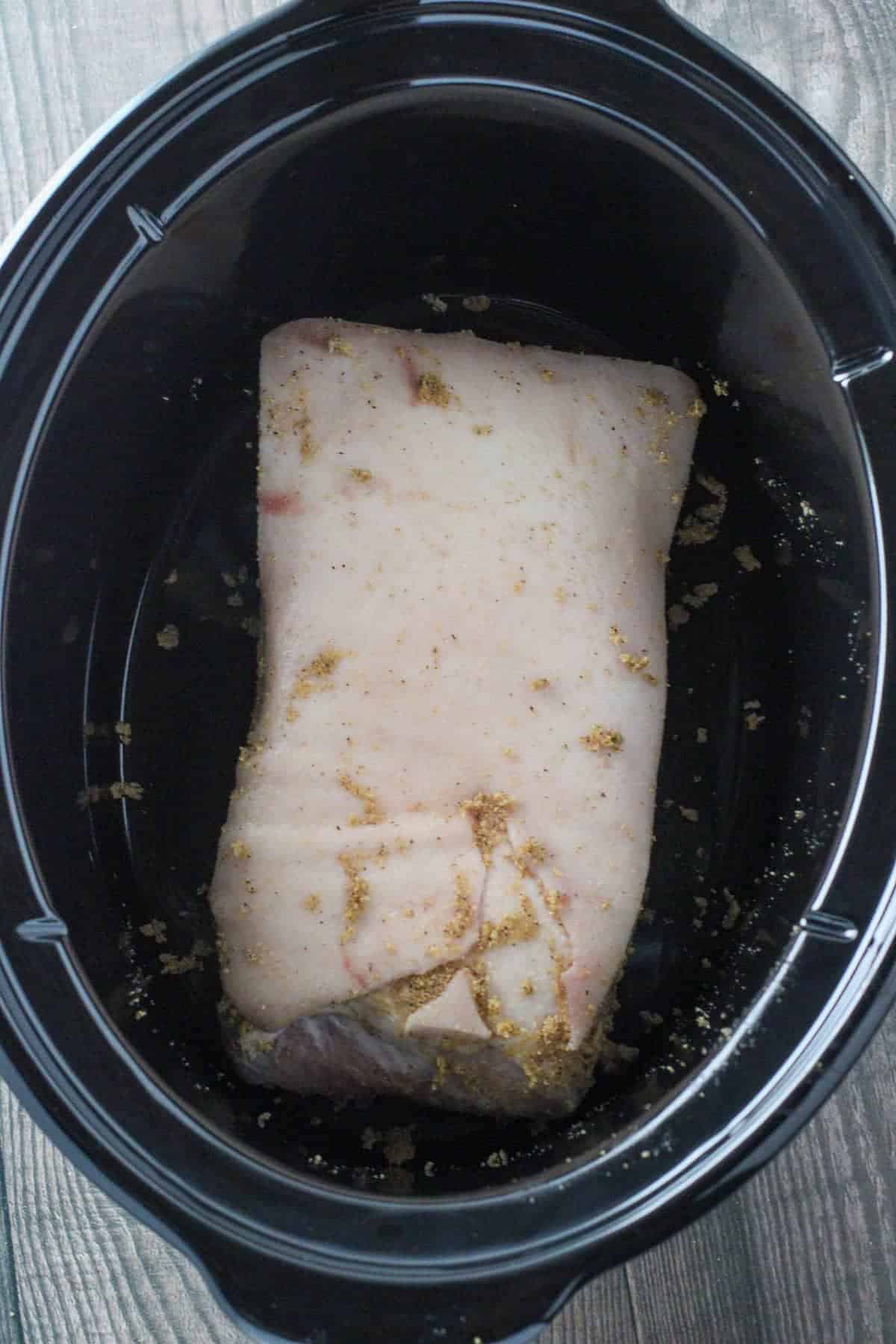 slab of seasoned pork belly in a black slow cooker