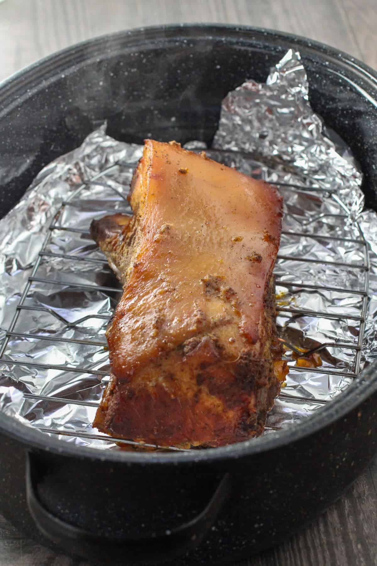 slow-cooker pork belly on a wire rack inside a foil-lined roasting pan