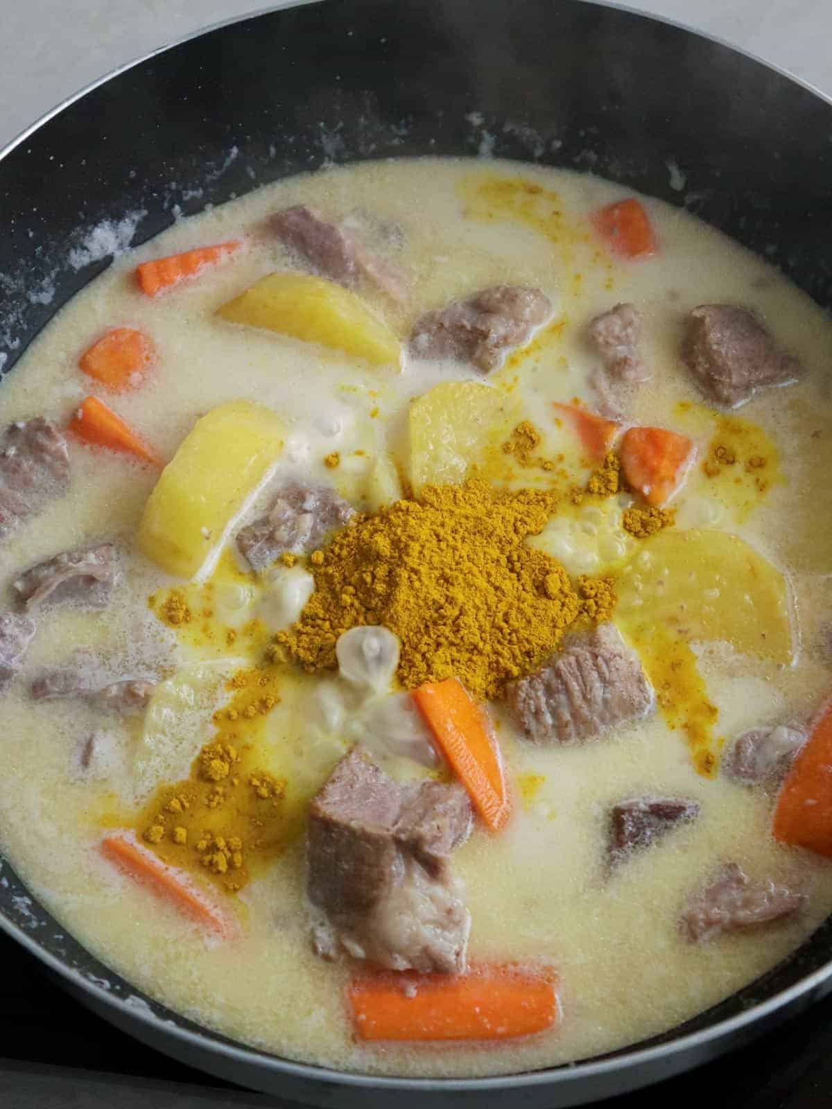 stirring curry powder into a pan of coconut beef curry