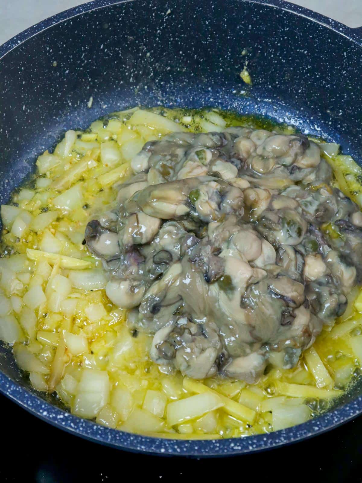 sauteing oysters with onions, ginger, and garlic in a pan