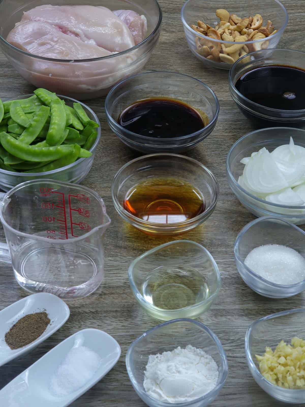 chicken, cashews, snow peas, oyster sauce, soy sauce, Chinese cooking wine, garlic, onions, salt, pepper, oil, water in bowls