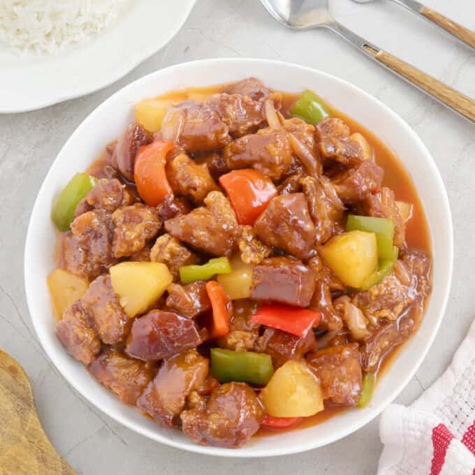 Sweet and Sour Pork in a serving bowl with a plate of steamed rice on the side