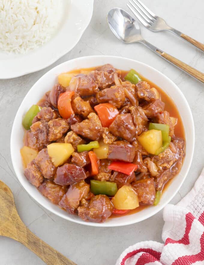 Sweet and Sour Pork in a serving bowl with a plate of steamed rice on the side