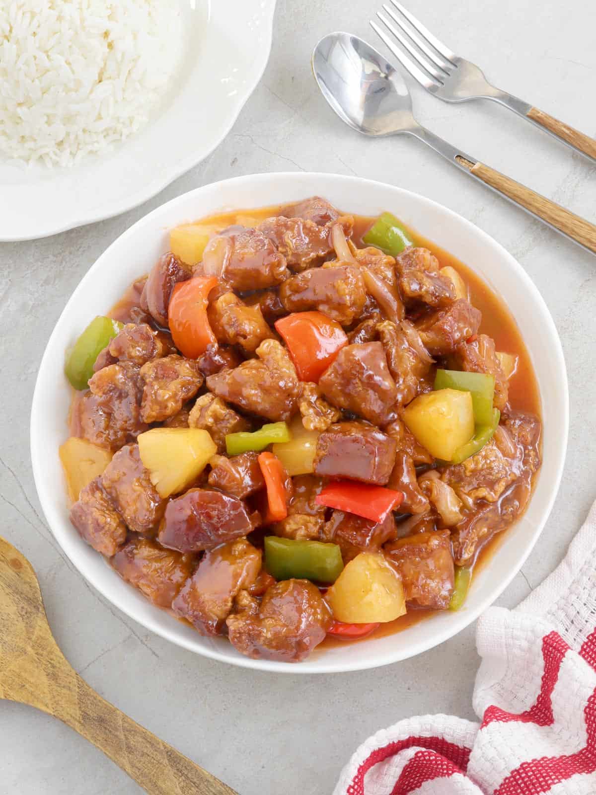 Sweet and Sour Pork in a serving bowl with a plate of steamed rice on the side