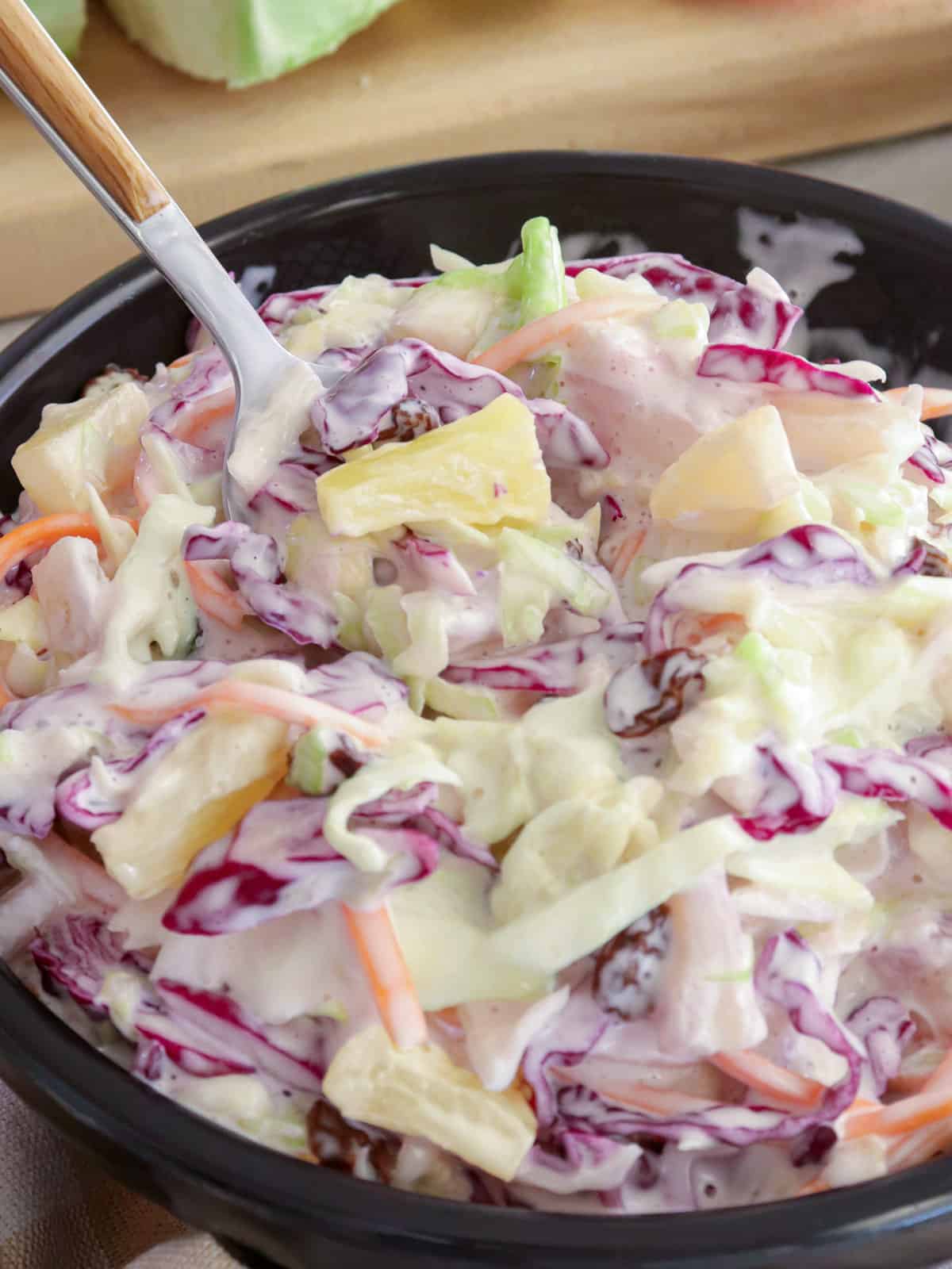 serving tropical coleslaw with pineapples from a black bowl.