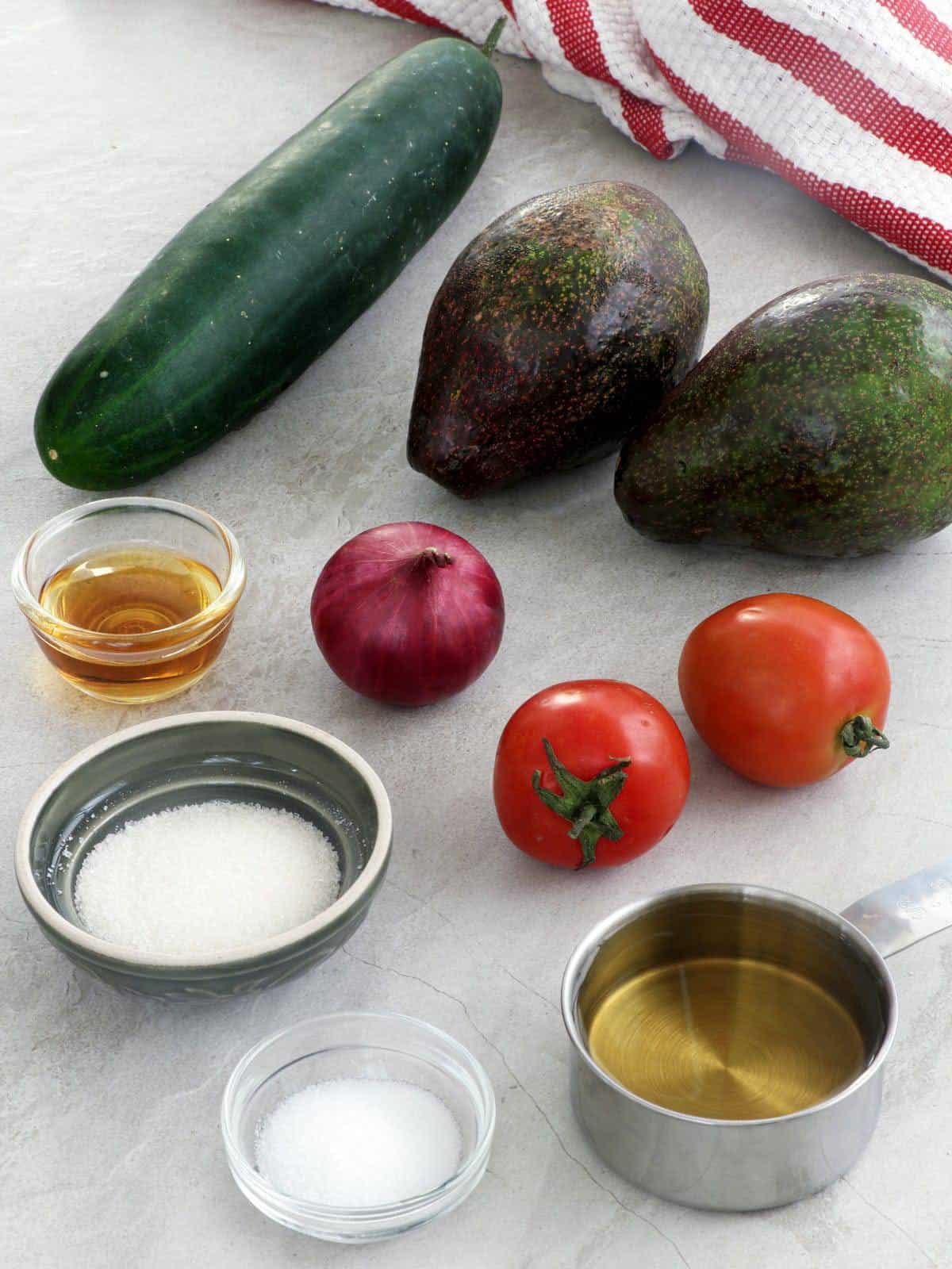 Cucumber, avocadoes, tomatoes, red onion with salt, pepper, oil, sugar in bowls