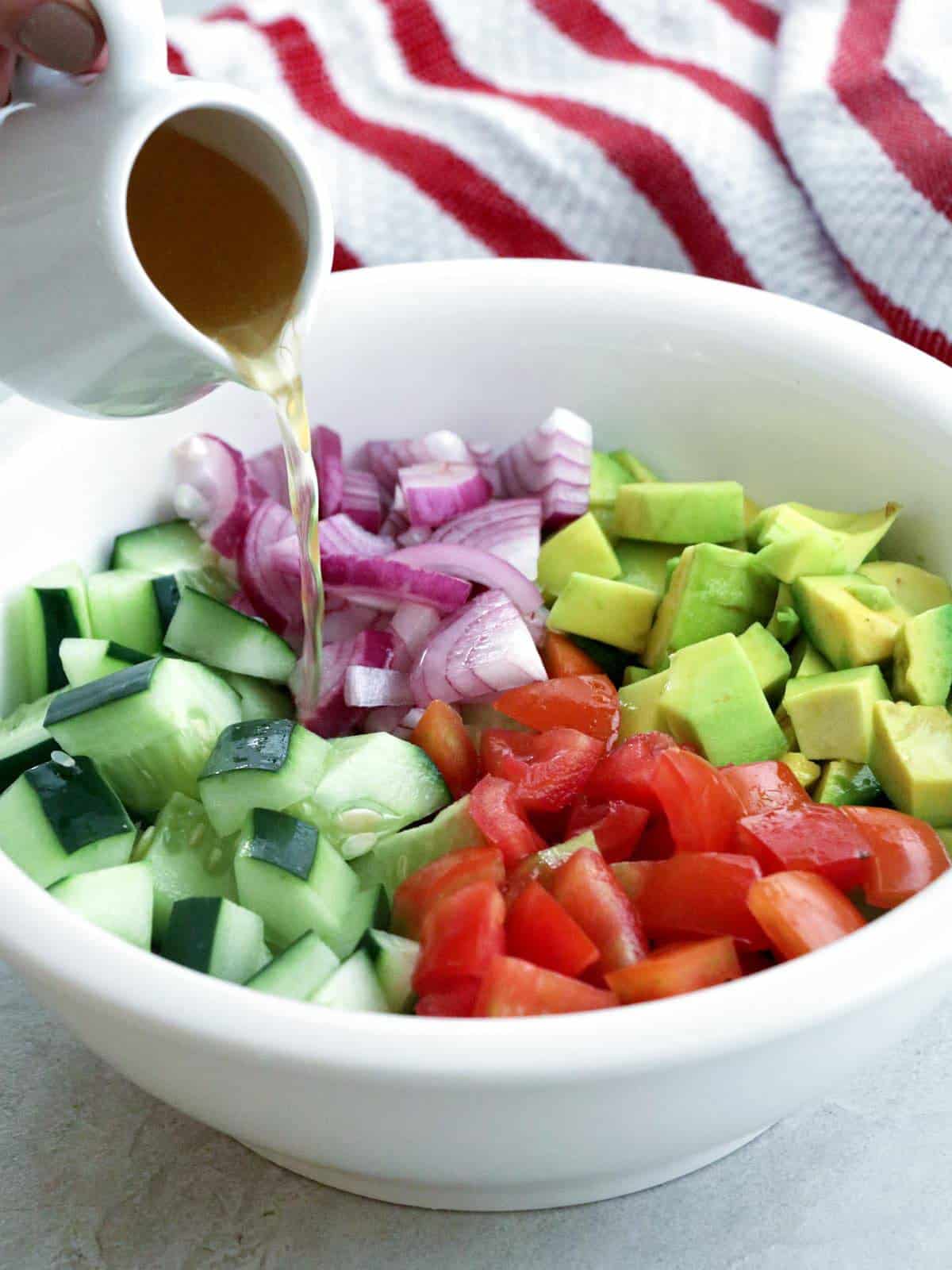 pouring rice vinegar dressing on diced cucumber, tomatoes, avocados, and red onions