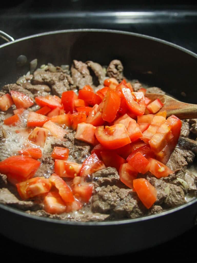 cooking sliced beef and tomato stew in a pan