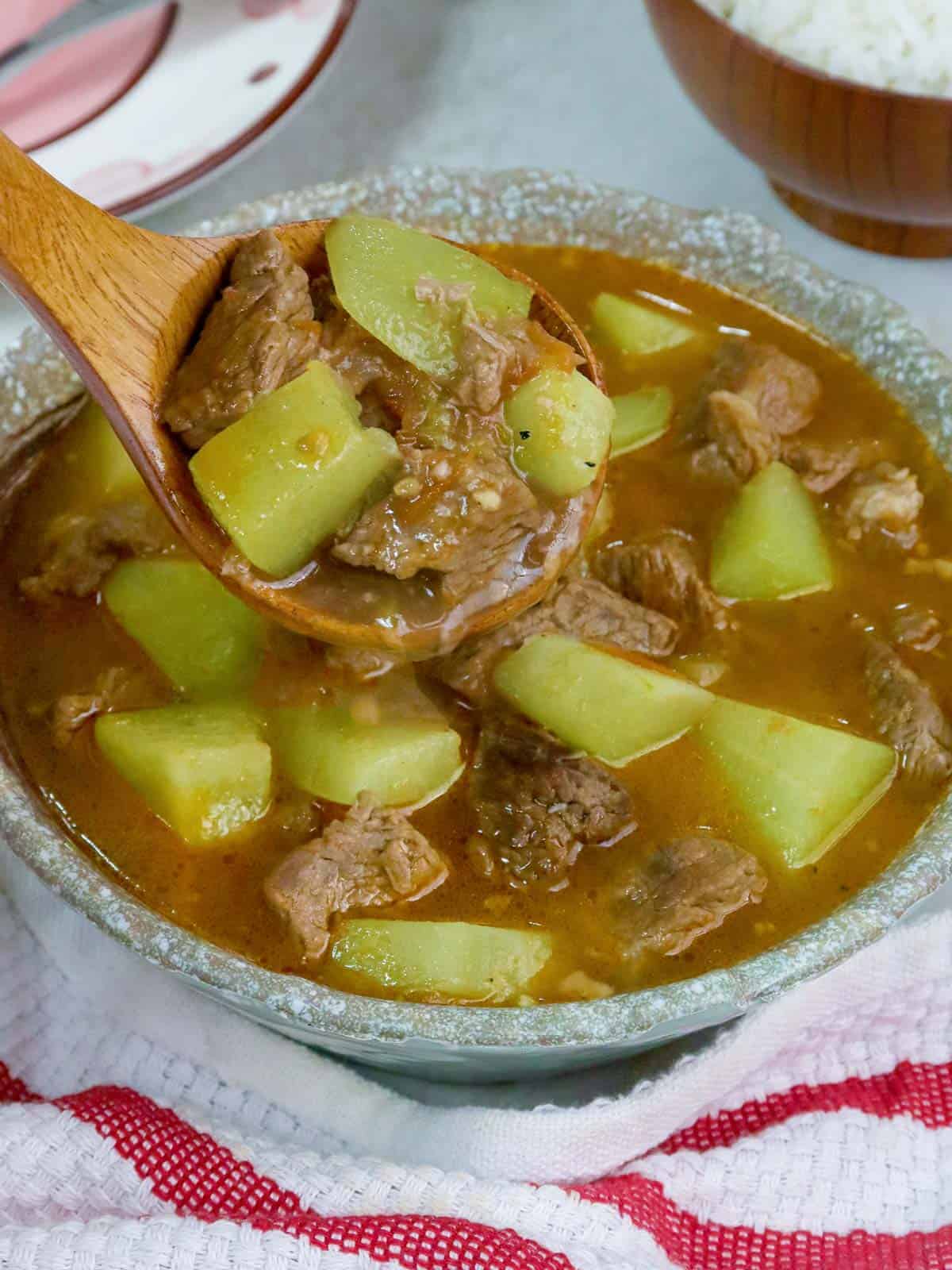 serving Filipino-style Beef and Chayote soup with a wooden ladle from a bowl