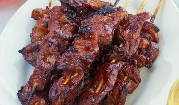 filipino pork barbecue on a stick on a white serving platter