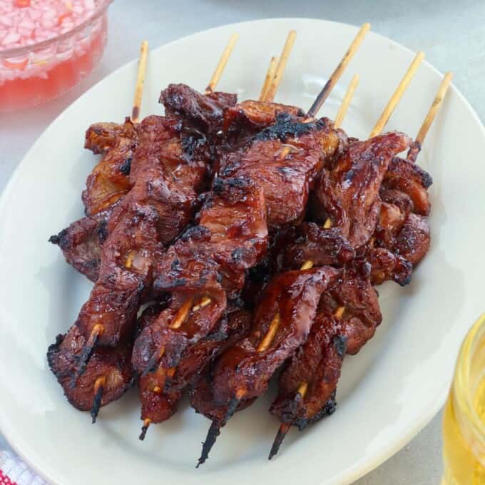 filipino pork barbecue on a stick on a white serving platter