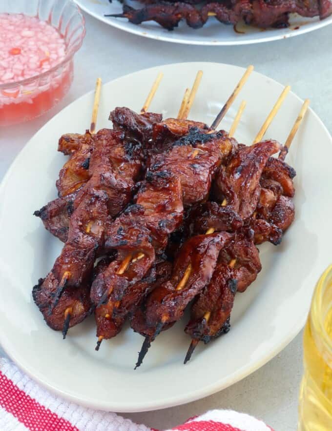 filipino pork barbecue on a stick on a white serving platter