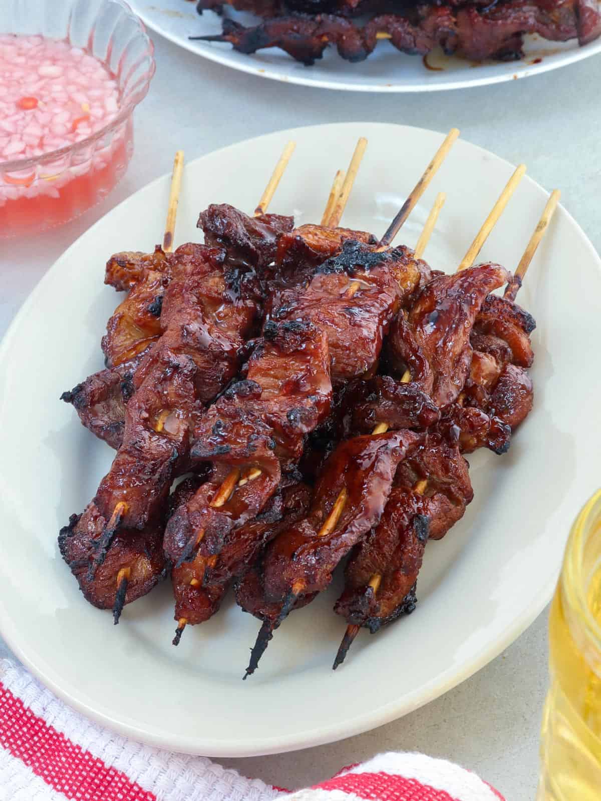 filipino pork barbecue on a stick on a white serving platter