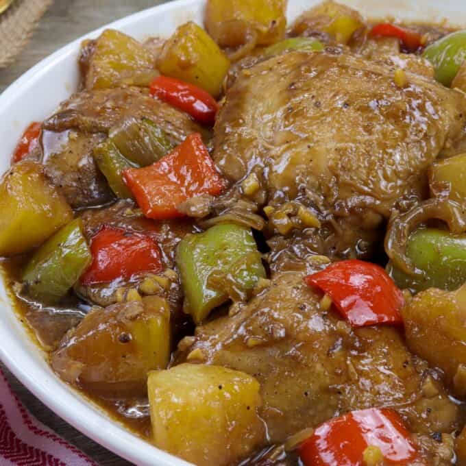 Hawaiian Chicken in a white serving bowl with a plate of steamed rice in the background.