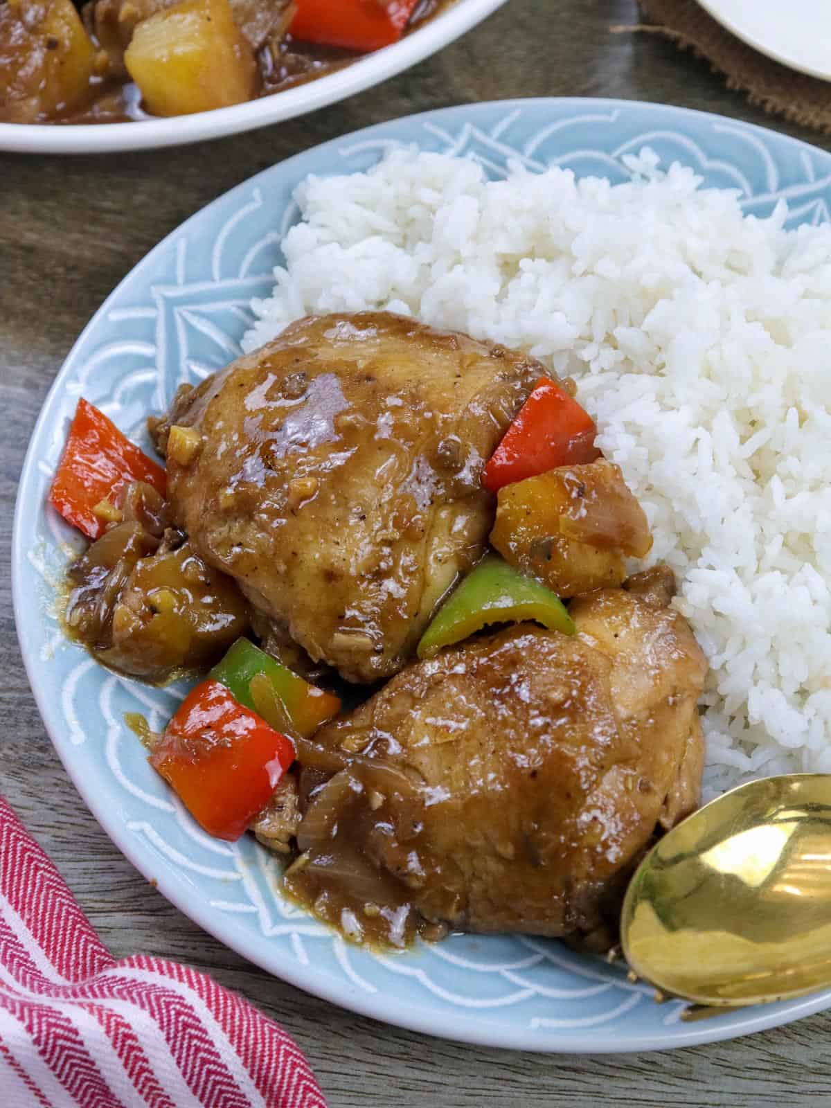 Pineapple chicken thighs on a blue serving plate with a side of steamed rice.