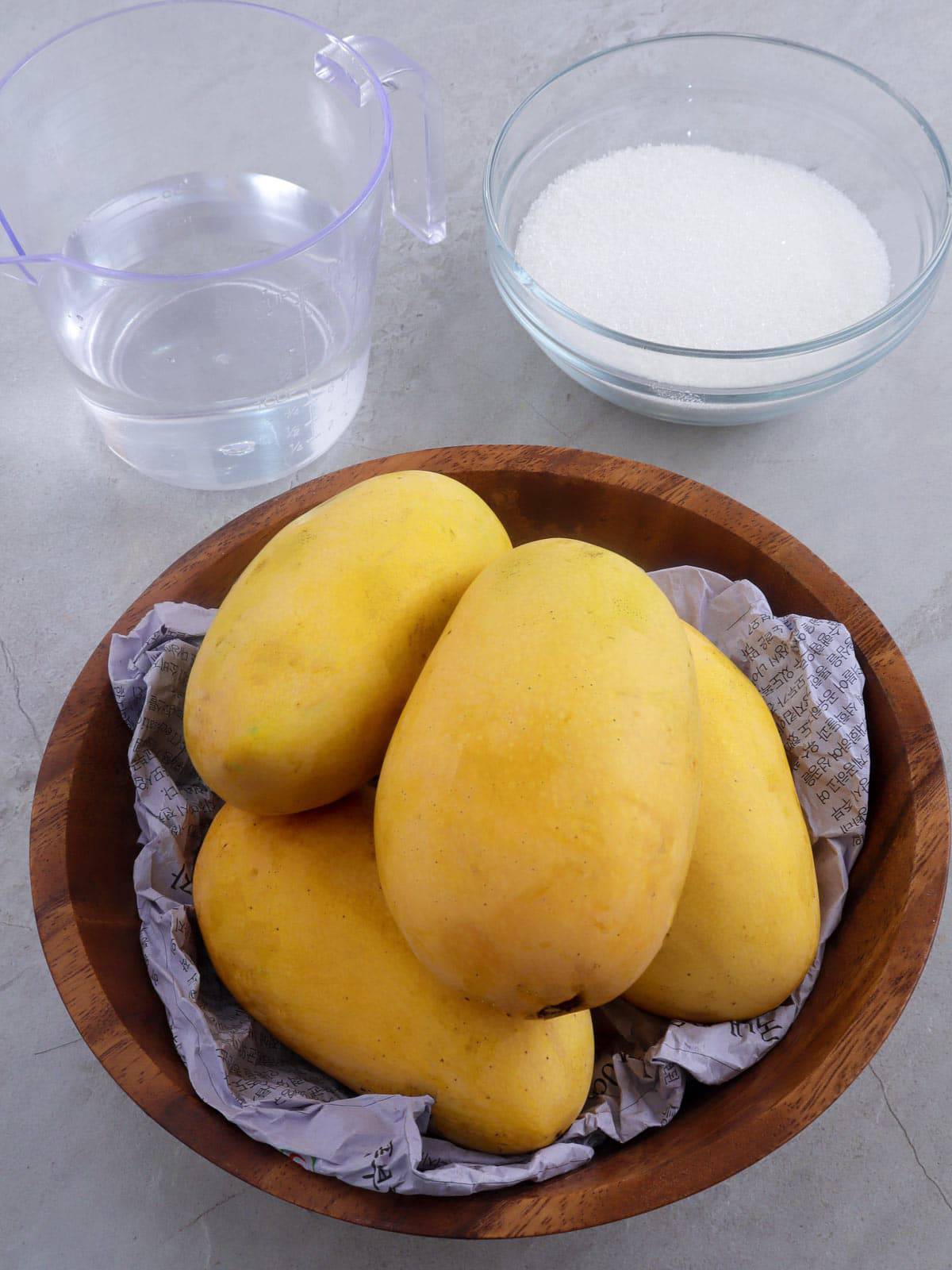 Manila mangoes in a brown bowl with a a glass of water and a bowl of sugar on the side