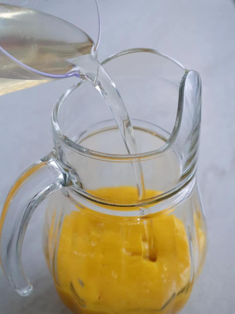 adding simple to mango pulp in a glass pitcher