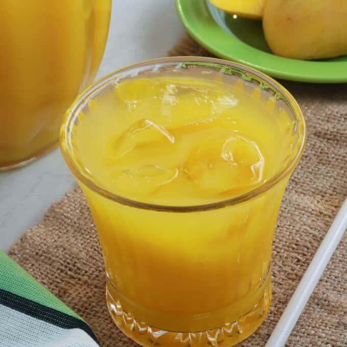 mango juice in a clear glass with pitcher on the side
