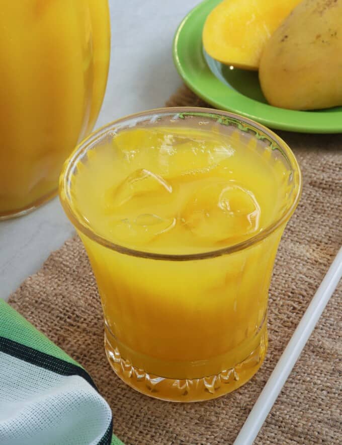 mango juice in a clear glass with pitcher on the side