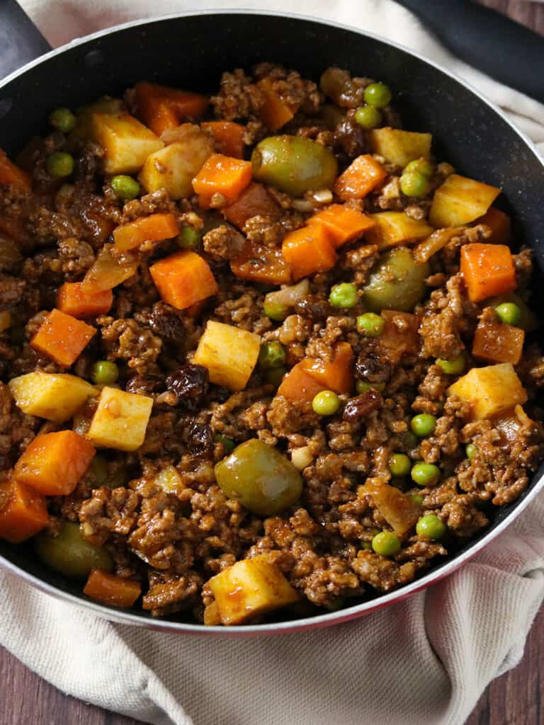 picadillo with potatoes, carrots, raisins, olives, green peas, and thick tomato sauce in a skillet