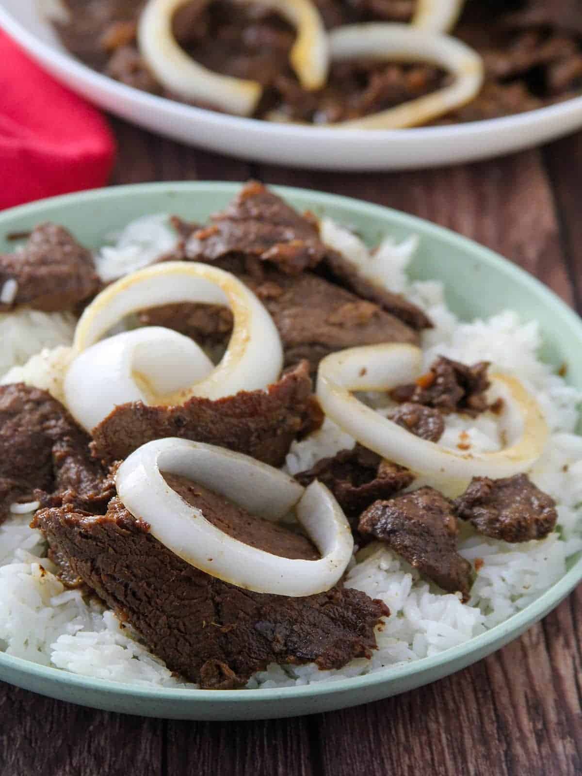 bistek Tagalog with onions over rice on a serving plate