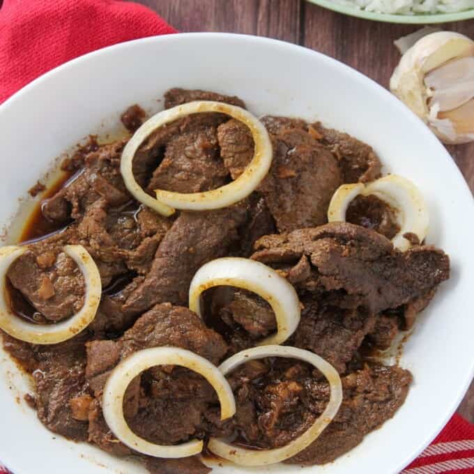 Filipino beefsteak with onions in a white serving bowl