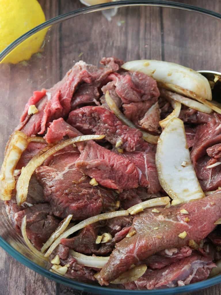 marinating beef slices with onions, garlic, soy sauce, and lemon juice in a glass bowl