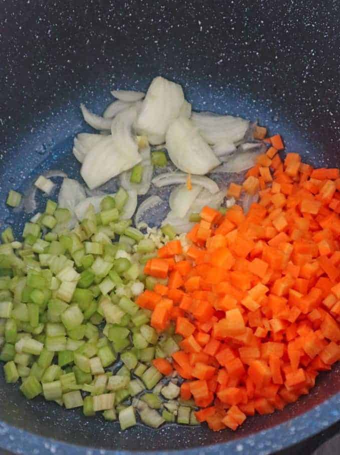 sauteeing diced celery, diced carrots, and sliced onions in a pot