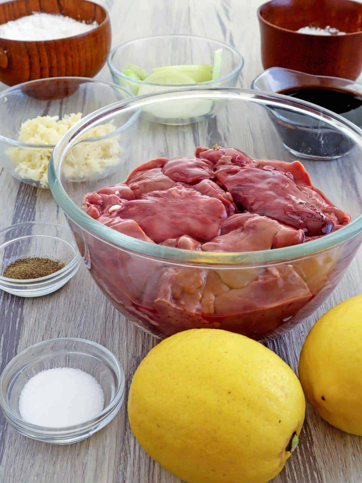 chicken livers in a bowl and lemons, cornstarch, flour, salt, soy sauce, minced garlic, and onions in small bowls on the side