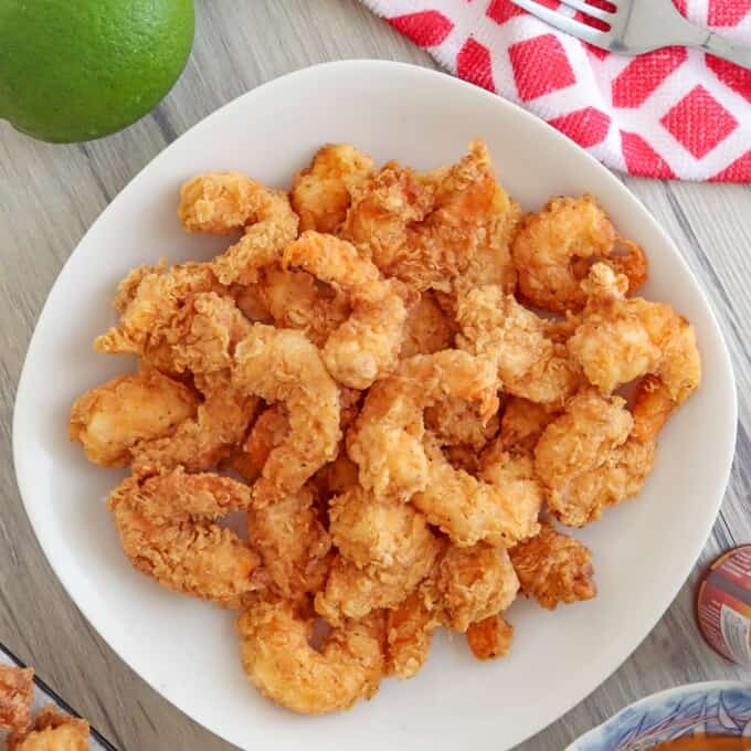 breaded shrimp in a white bowl with sliced limes and a bowl of sweet and sour sauce on the side
