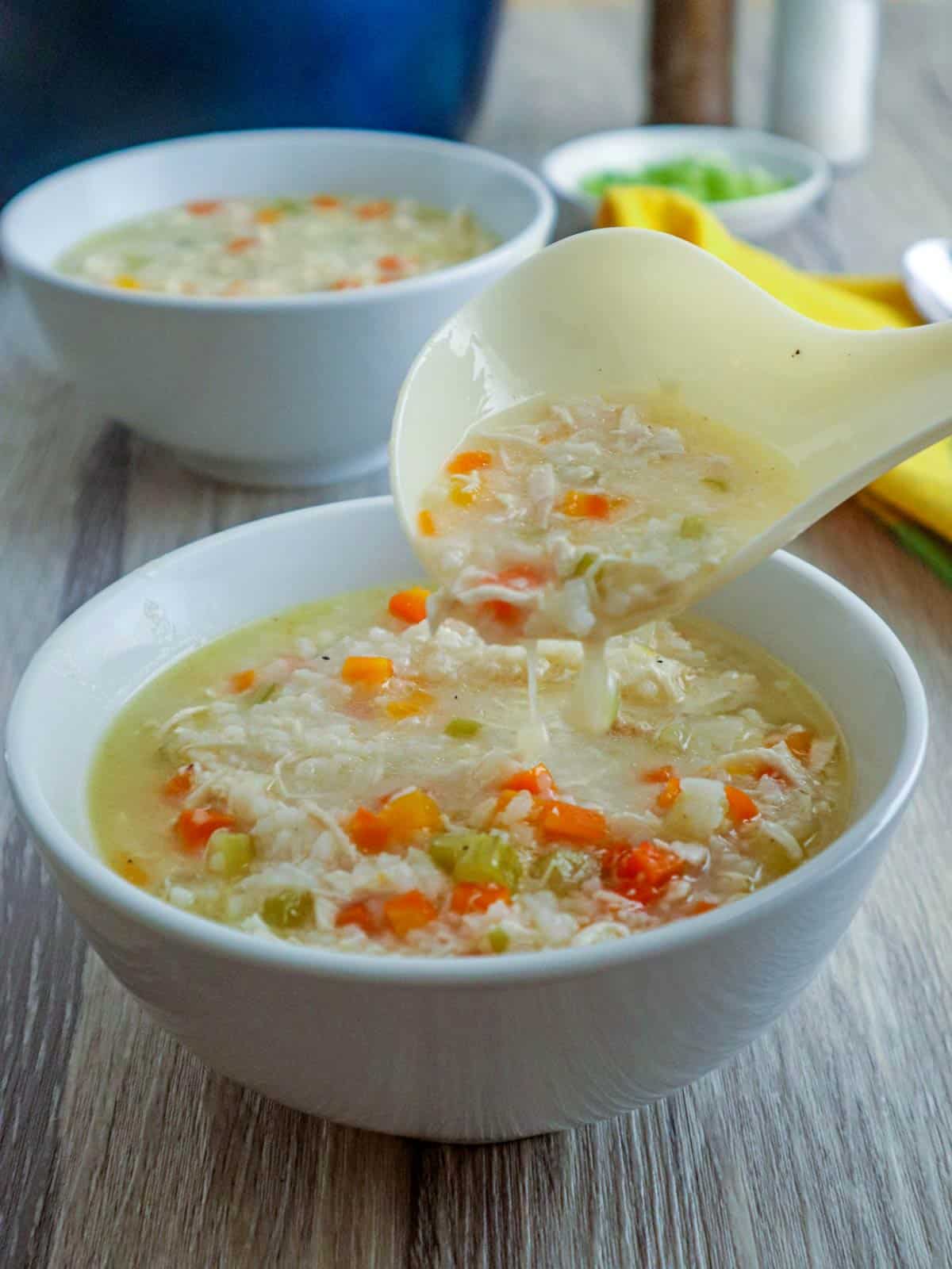serving chicken rice soup into a bowl with a ladle