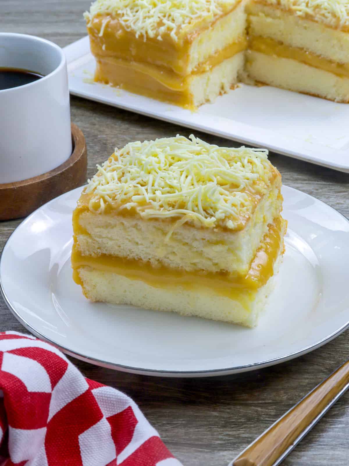 slice of yema cake on a serving plate with a cup of coffee in the background.