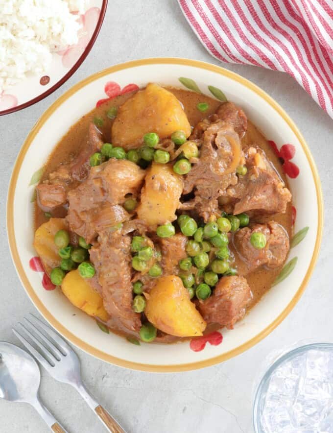 Sinantomas in a white serving bowl with a plate of steamed rice on the side