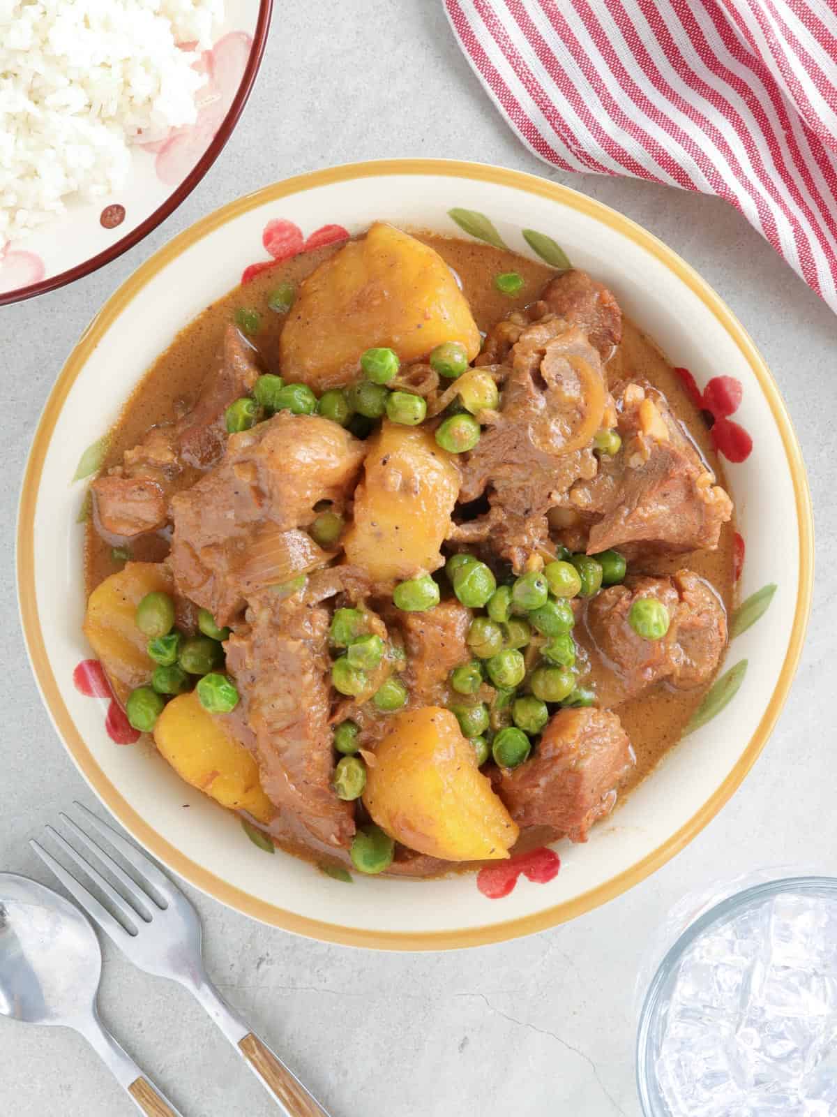 Sinantomas in a white serving bowl with a plate of steamed rice on the side