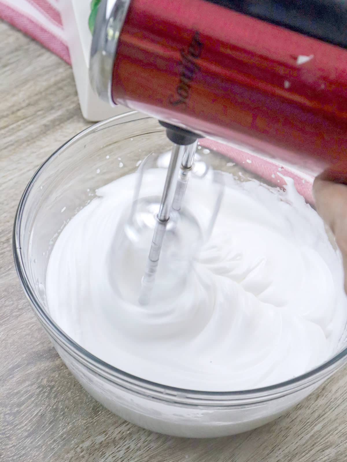 whipping eggs into meringue in a bowl with a red hand mixer.