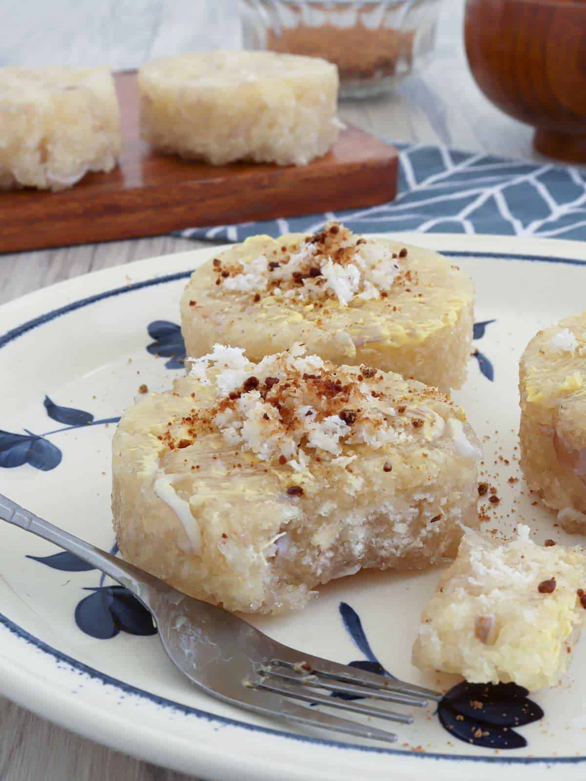 eating steamed cassava cakes topped with grated coconut on a plate