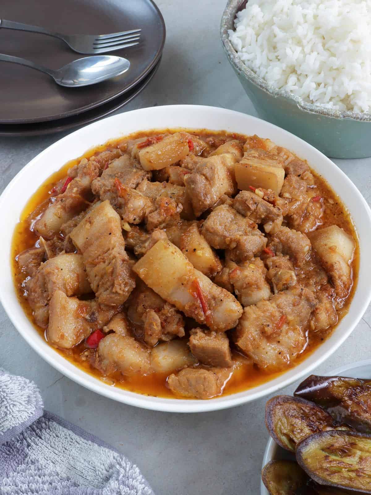 Binagoongan Baboy in a white serving bowl with side of fried eggplant and steamed rice