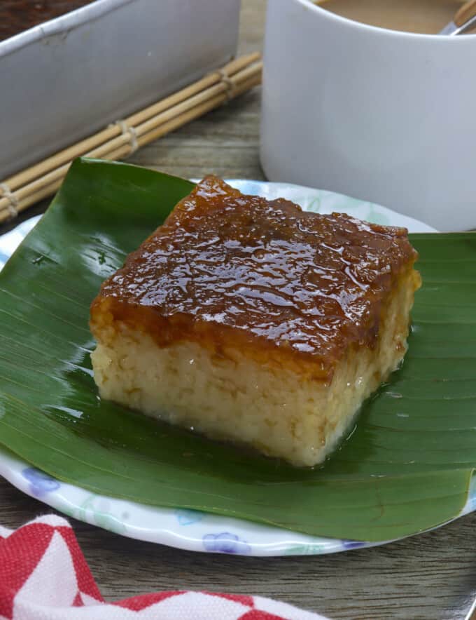 slice of bibingkang malagkit on a banana-lined white serving plate with cup of coffee in the bakcground.