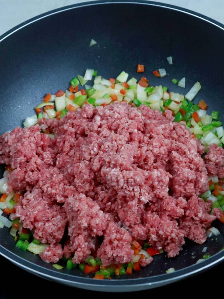 browning ground beef with bell peppers and onions in a pan