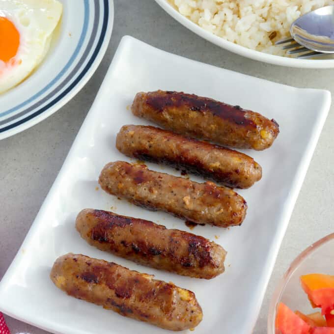 Skinless Longganisa on serving platter with plates of rice and fried eggs on the side