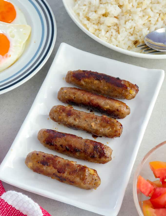 Skinless Longganisa on serving platter with plates of rice and fried eggs on the side