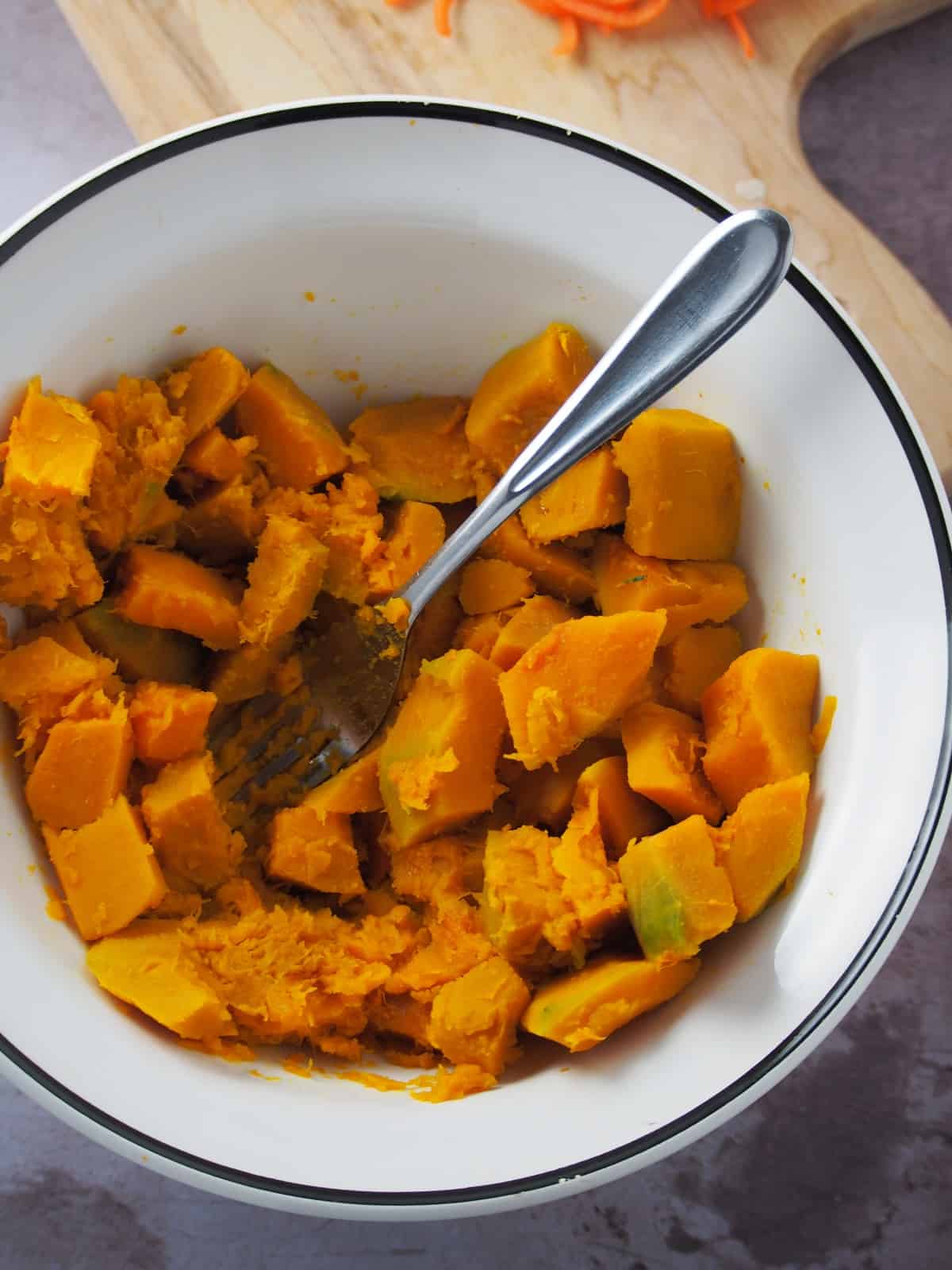 smashing cooked kalabasa cubes with a fork in a white bowl